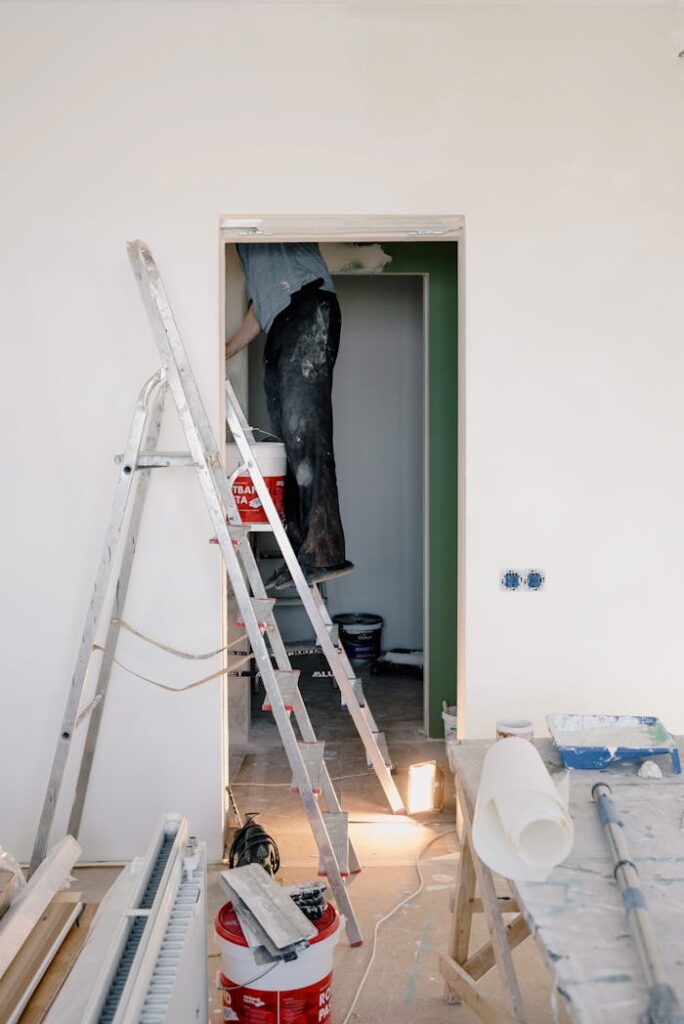 Indoor scene of home renovation with ladders, tools, and paint buckets.